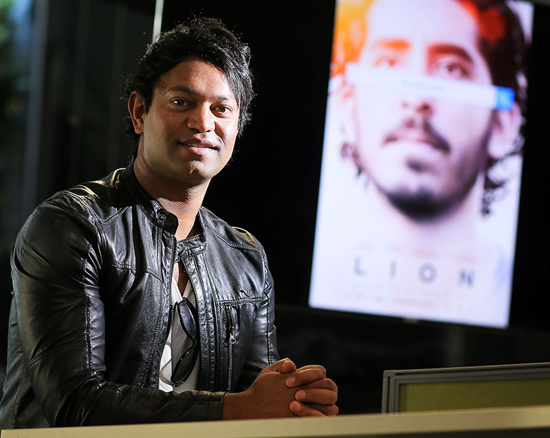 Saroo Brierley - Texas GIS Forum Keynote, speaking in front of map, picture of his book on right